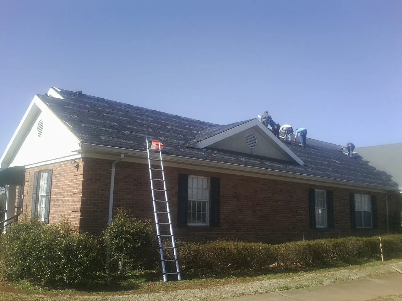 Crew tearing shingles off a brick ranch roof with a ladder set — Emergency Roof Repair work by our crew in Rocky Face