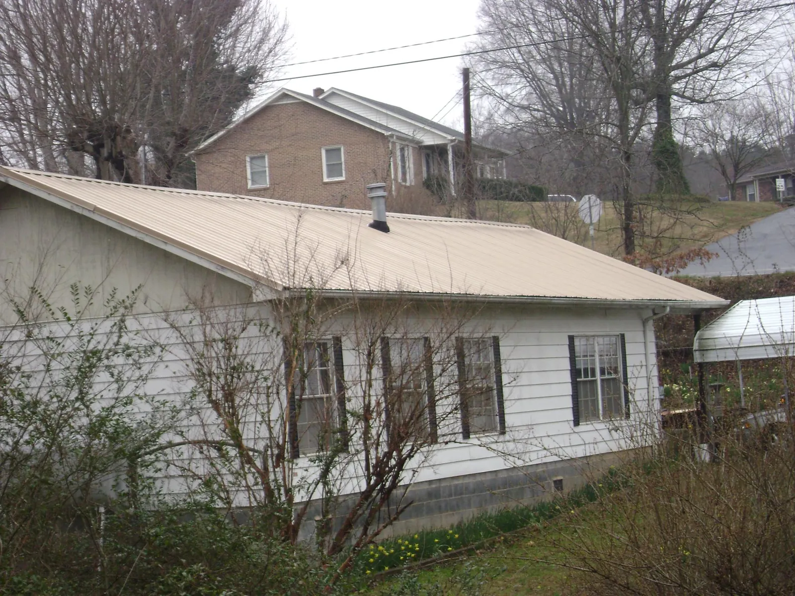Tan metal roof on a white sided house set into a hillside — Commercial Roofing by Roofing Brothers in Rocky Face